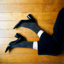 Vrouw draagt zwarte Klue glittersokken met hakken, elegante glans in duurzaam bamboe met luxueuze afwerking.